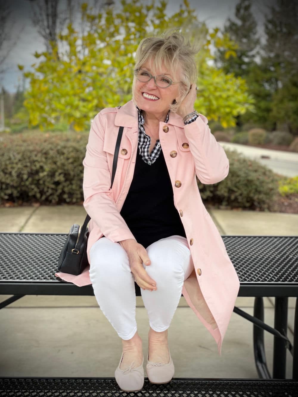 woman sitting on picnic table wearing pink trenmch coat and white jeans