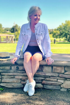 blonde woman sitting on wall wearing white denim jacket and striped tee