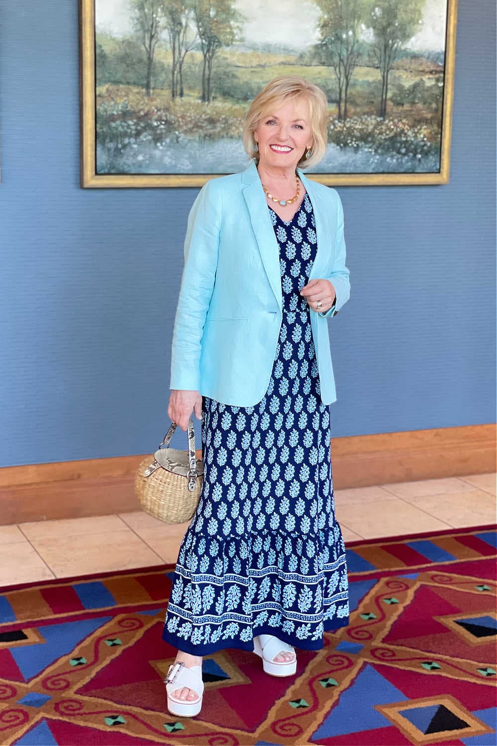 blonde woman wearing aqua blazer over paisley dress in front of blue wall