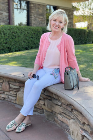 over 50 blogger sitting on wall in white jeans and pink cardigan