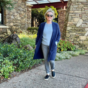 blonde woman walking wearing long blue cardiigan over blue sweater and gray jeans