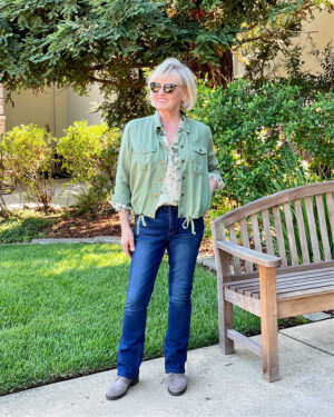 woman wearing blue jeans, suede boots, green jacket and floral shirt for warmer fall days