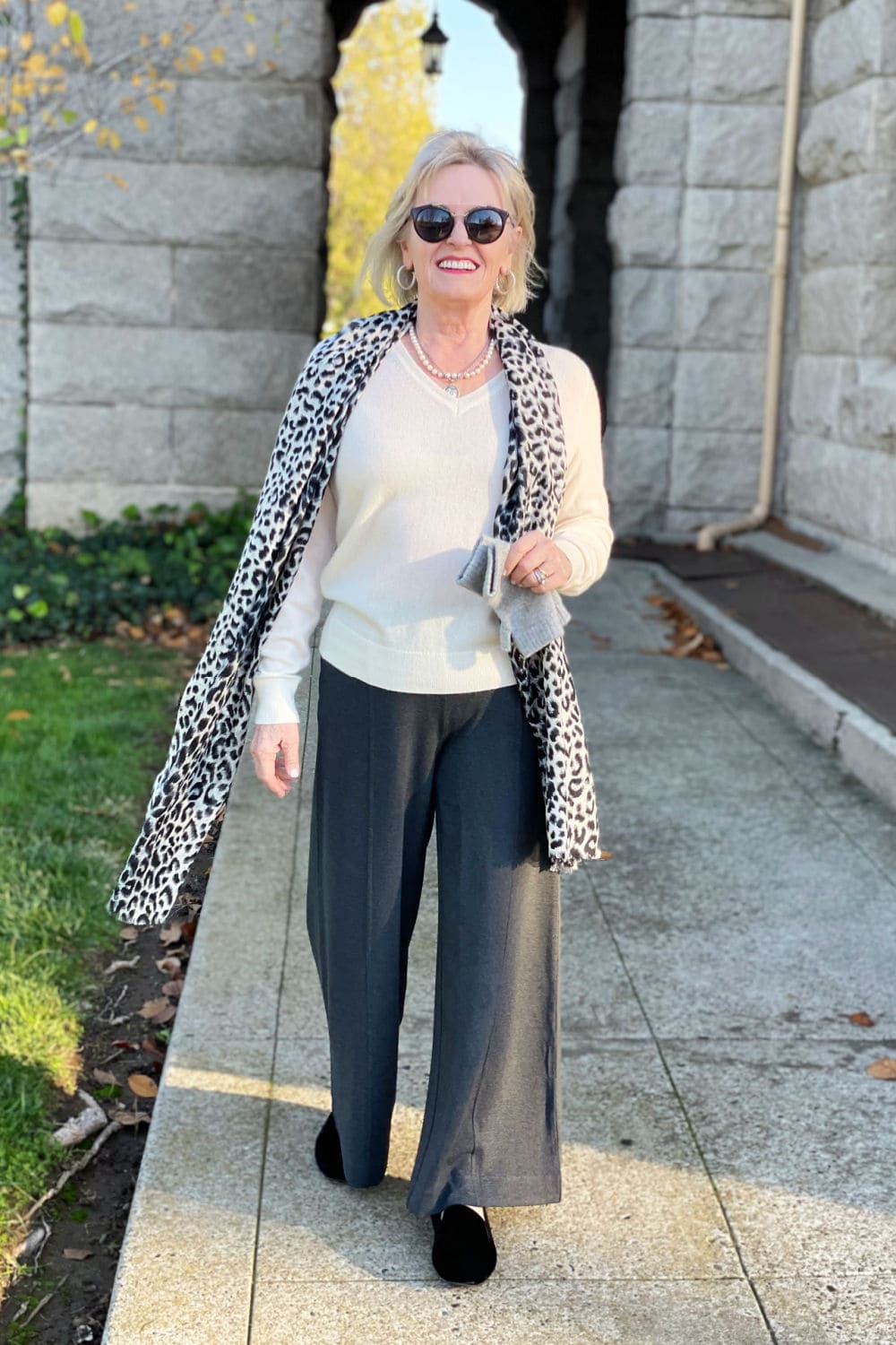woman walking in gray pants and cream cashmere sweater with leopard scarf