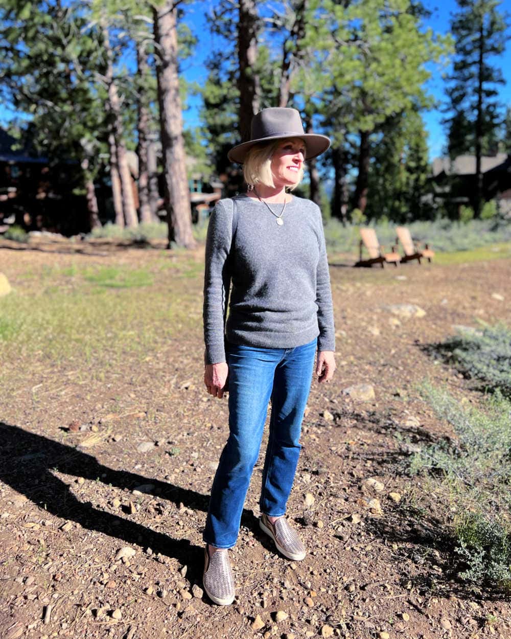woman wearing paige jeans outfit with cashmere sweater and grey fedora in forest