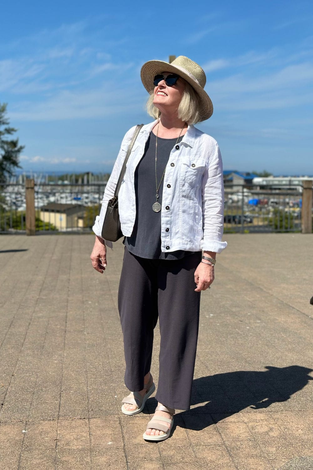 woman on dock wearing straw hat, white jacket, grey tank and pants with Ecco sandals