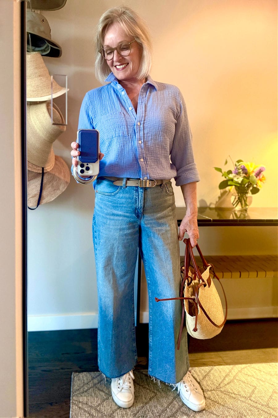 Woman over 60 wearing polished casual summer outfit with cotton gauze shirt, wide-leg crop jeans, and basket bag