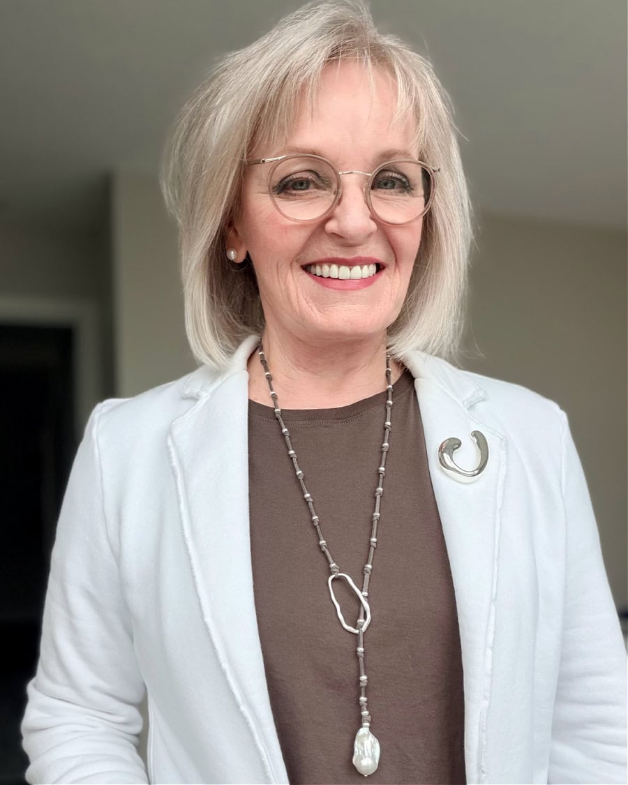 women  layering pearl stud earrings with silver brooch and pearl lariat necklace while wearing sweatshirt blazer
