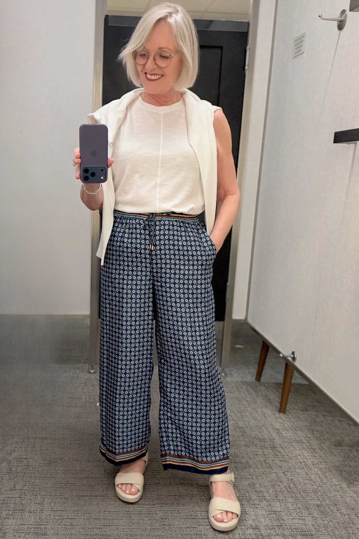 Travel-friendly summer outfit with navy geometric print drawstring pants, a white tank, and a cardigan over the shoulders.