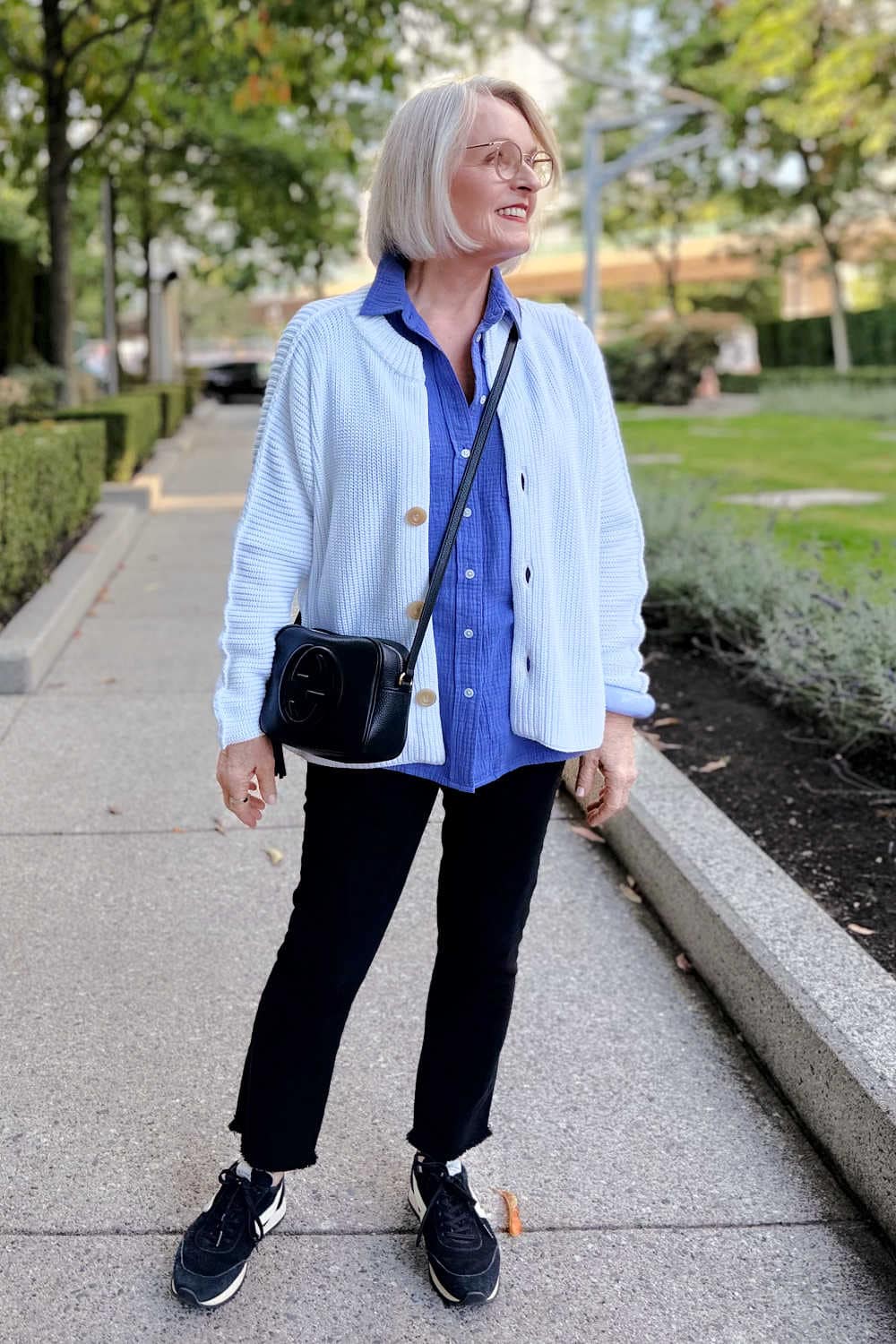 Real woman wearing white sweater, purple shirt and black jeans.