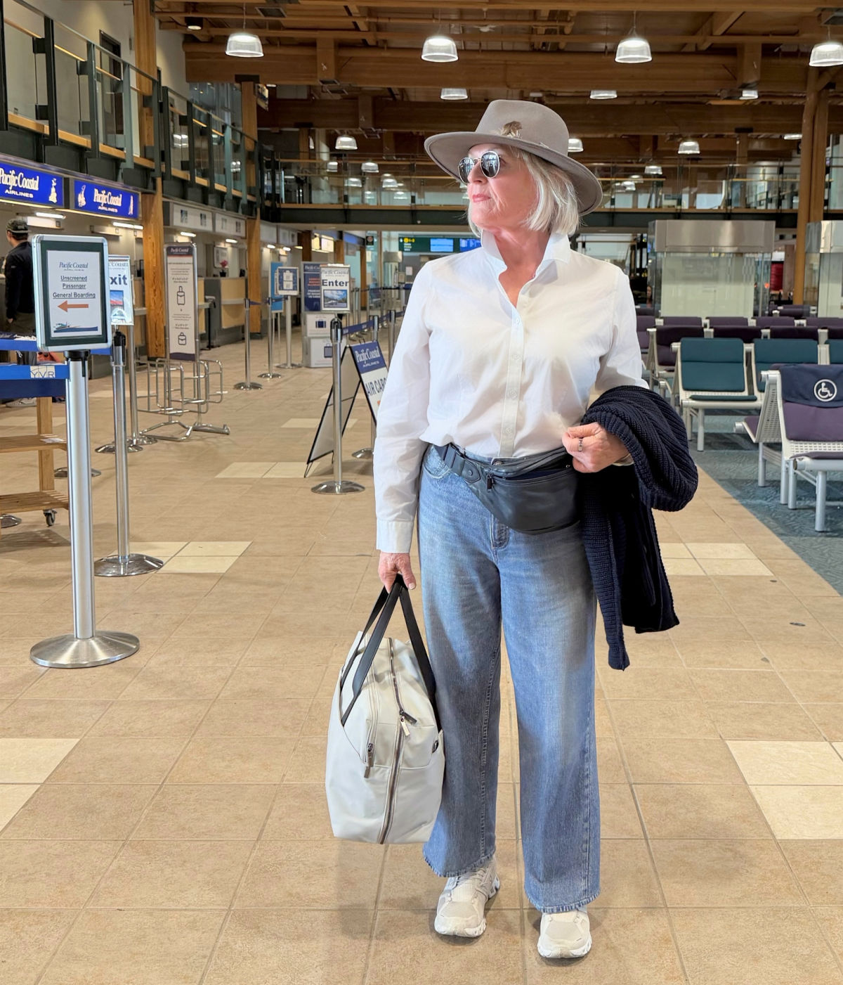 WOMAN IN AIRLINE TERMINAL WEARING WHITE SHIRT, STRETCH MIRAMAR JEANS AND COMFY SNEAKERS