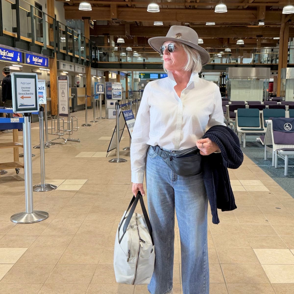 WOMAN OVER 50 AT AIRPORT WEARING NO IRON WHITE SHIRT, STRETCY JEANS AND COMFORTABLE SNEAKERS TO BOARD HER FLIGHT